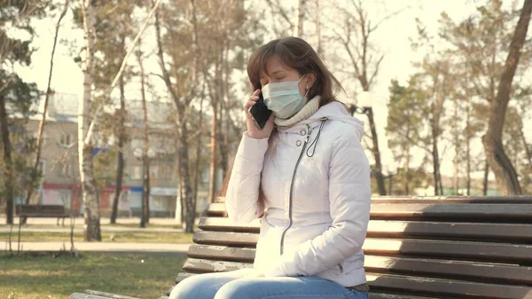 Έννοια της υγείας και της ασφάλειας. νέα γυναίκα με ιατρική προστατευτική μάσκα κάθεται με ένα smartphone στο δρόμο της πόλης στην Ευρώπη. Προστασία από τον ιό του κερατοειδούς. τουρίστες στο δρόμο φορούν προστατευτική μάσκα από ιούς. — Φωτογραφία Αρχείου