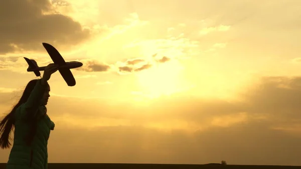 Chica feliz corre con un avión de juguete en un campo en la luz del atardecer. niños juegan juguete avión. adolescente sueña con volar y convertirse en piloto. chica quiere convertirse en piloto y astronauta. Movimiento lento — Foto de Stock