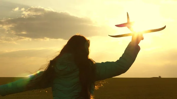 Lycklig flicka springer med ett leksaksplan på ett fält i solnedgångens sken. Barn leker leksaksflygplan. Tonåringen drömmer om att flyga och bli pilot. Hon vill bli pilot och astronaut. Långsamma rörelser — Stockfoto