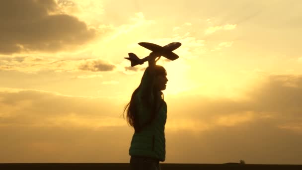 幸せな女の子は日没の光の中でフィールド上のおもちゃの飛行機で実行されます。子供はおもちゃの飛行機で遊ぶ。10代の頃はパイロットになる夢を見ました。女の子はパイロットと宇宙飛行士になりたい。スローモーション — ストック動画