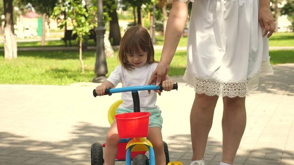 Konzept einer glücklichen Familie und Kindheit. Eltern und kleine Tochter spazieren im Park. Glückliche Mutter bringt ihrer kleinen Tochter das Fahrradfahren bei. Mutter spielt mit ihrem Baby im Freien. Kind lernt Fahrradfahren. — Stockfoto