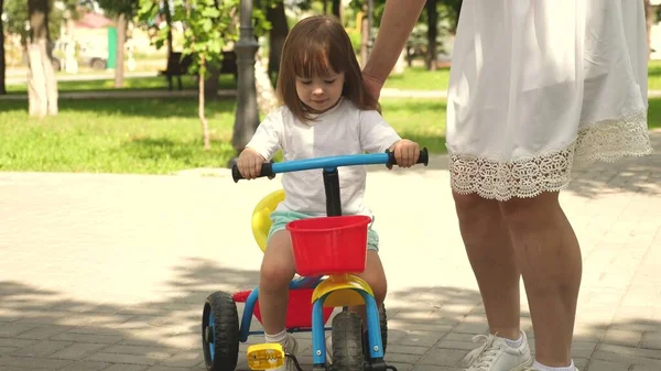 Mutlu aile ve çocukluk kavramı. Ebeveynler ve küçük kızları parkta yürürler. Mutlu anne küçük kızına bisiklet sürmeyi öğretiyor. Anne bebeğiyle dışarıda oynuyor. Çocuk bisiklet sürmeyi öğreniyor.. — Stok fotoğraf