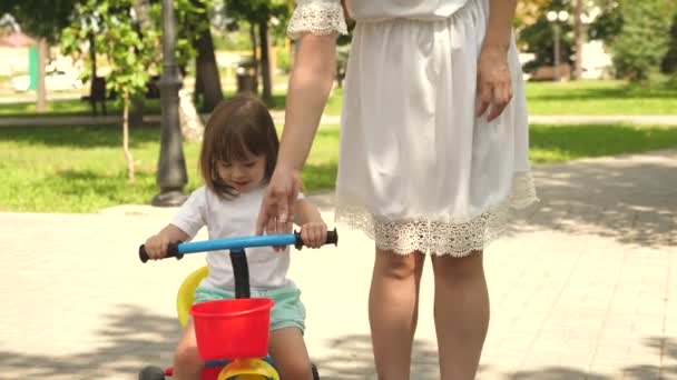 Mutlu aile ve çocukluk kavramı. Ebeveynler ve küçük kızları parkta yürürler. Mutlu anne küçük kızına bisiklet sürmeyi öğretiyor. Anne bebeğiyle dışarıda oynuyor. Çocuk bisiklet sürmeyi öğreniyor.. — Stok video