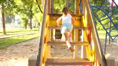 Çocuk merdivenlerden çıkıp çocuklar kayıyor. Anne ve bebek oyun bahçesinde oynuyorlar. Mutlu çocukluk kavramı. Mutlu çocukluk ve aile kavramı. Küçük çocuk gülüyor ve parkta oyun oynamaktan hoşlanıyor.