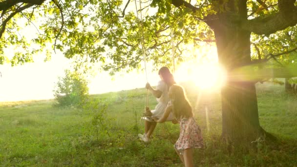 Kinderen die schommelen op een eiken tak in de zon. Dromen van vliegen. concept van een gelukkige jeugd. Mooie meisjes spelen in het park. tieners genieten van vliegen op swing op een zomeravond in het bos — Stockvideo