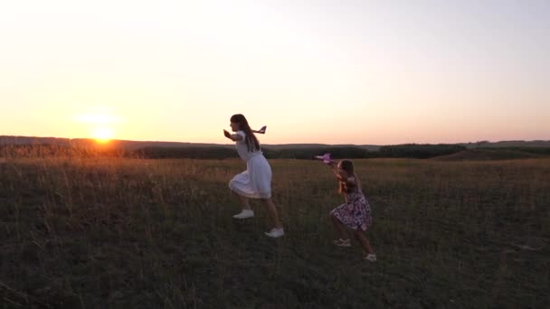 Healthy Children in meadow with an airplane in his hand. Dreams of flying. concept of happy childhood. Two free girls play with toy airplane on field. Silhouette of children playing on an airplane. — Stock Video