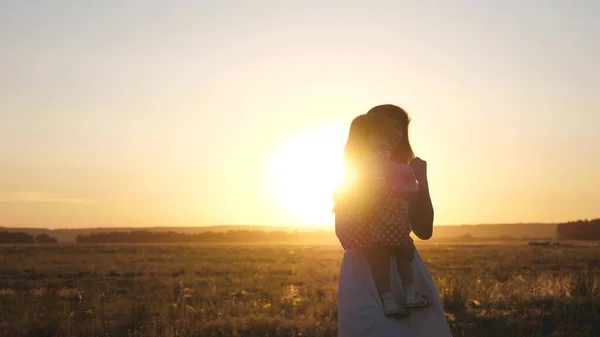 Maman libre et petite fille dansent au coucher du soleil. Mère et bébé en bonne santé dans ses bras dans le champ. concept d'une enfance heureuse. enfant heureux joue avec sa mère au coucher du soleil. concept de famille heureuse — Photo