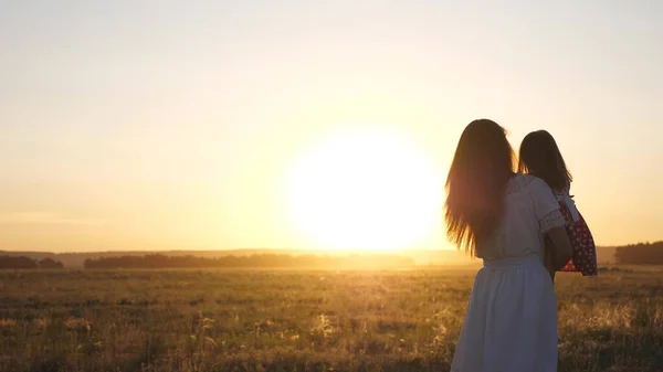 A mãe e a filha estão a dançar ao pôr-do-sol. Mãe e bebê saudável em seus braços no campo. conceito de uma infância feliz. criança feliz brinca com sua mãe ao pôr do sol. conceito de família feliz — Fotografia de Stock