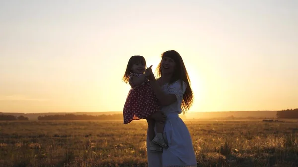 Maman libre et petite fille dansent au coucher du soleil. Mère et bébé en bonne santé dans ses bras dans le champ. concept d'une enfance heureuse. enfant heureux joue avec sa mère au coucher du soleil. concept de famille heureuse — Photo