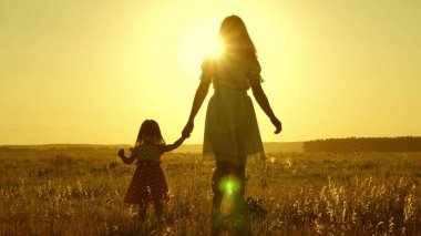 Özgür, çocuklu, mutlu bir aile kırsalda yürüyor. Sağlıklı anne ve bebek parkta dinleniyor. Mutlu çocukluk. Küçük kız ve anne el ele tutuşarak tarlada yürüyorlar. Bebek annesinin elini tutuyor..