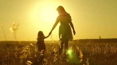 Özgür, çocuklu, mutlu bir aile kırsalda yürüyor. Sağlıklı anne ve bebek parkta dinleniyor. Mutlu çocukluk. Küçük kız ve anne el ele tutuşarak tarlada yürüyorlar. Bebek annesinin elini tutuyor..