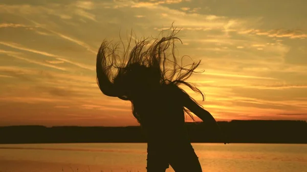 Chica libre bailando al atardecer con el pelo largo en los rayos de la puesta del sol. mujer sana bailando en la fiesta de la playa. Baile de noche en la orilla del mar. En cámara lenta. chica viajero, turista está bailando —  Fotos de Stock