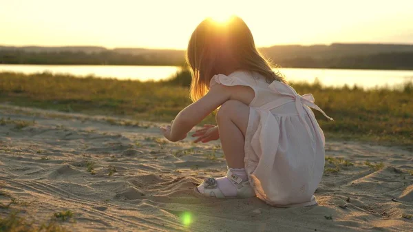 Здоровый ребенок играет на песке на пляже. счастливая маленькая девочка играет в парке на солнце. Концепция отпуска и путешествия. ребенок летом на лугу. Маленькая дочь берет песок в руки и идет сквозь дрожь . — стоковое фото