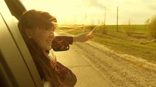 Donna libera viaggia in auto cattura il vento con la mano dal finestrino dell'auto. Ragazza con i capelli lunghi è seduto sul sedile anteriore della macchina, allungando il braccio fuori finestra e la cattura bagliore del sole al tramonto — Foto Stock