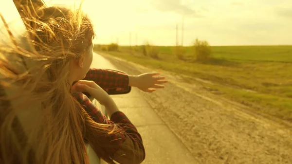 Donna libera viaggia in auto cattura il vento con la mano dal finestrino dell'auto. Ragazza con i capelli lunghi è seduto sul sedile anteriore della macchina, allungando il braccio fuori finestra e la cattura bagliore del sole al tramonto — Foto Stock