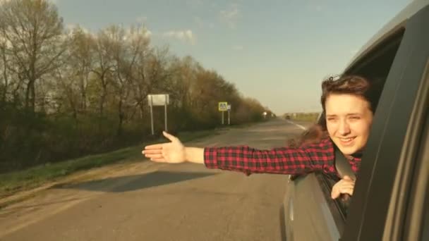 Donna libera viaggia in auto cattura il vento con la mano dal finestrino dell'auto. Ragazza con i capelli lunghi è seduto sul sedile anteriore della macchina, allungando il braccio fuori finestra e la cattura bagliore del sole al tramonto — Video Stock