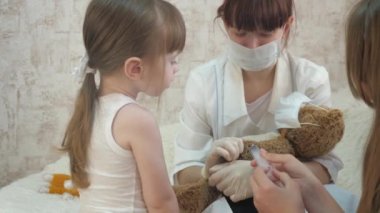 Çocuklar koruyucu bir maskenin içinde tıbbi bir şırıngayla oynarlar. Oyun doktor gibi davranır, hemşire, hastayı aşıyla tedavi eder. Sağlıklı küçük kız oyuncak ayı enjekte eder. Çocuk hastanede oynuyor..