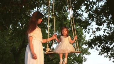Bir anne çocuğuyla oynuyor. Ormandaki bir meşe dalında ipte sallanıyorlar. Özgür aile Park 'ta eğlenir. Anne sallanıyor sağlıklı küçük kız ağaçta güneşin altında sallanıyor..