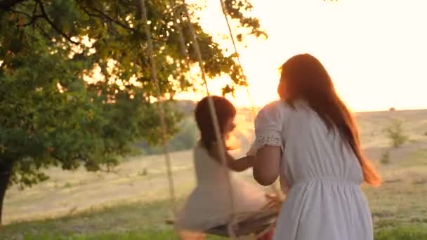 Une mère joue avec l'enfant ils se balancent sur une corde sur une branche de chêne dans la forêt. famille libre s'amuse dans le parc. mère roches saine petite fille sur balançoire sous arbre au soleil . — Video