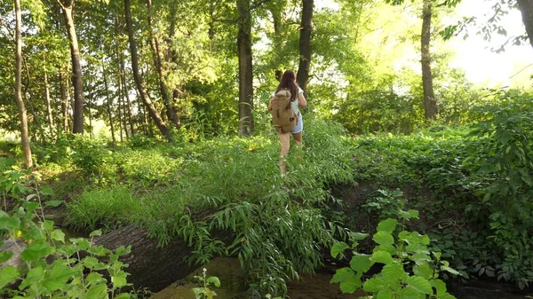 Vrije meidenreiziger steekt rivier over op een boomstam. Een meisje met een rugzak is gaan wandelen. jonge gezonde vrouwelijke toerist steekt de rivier over op omgevallen boom. man op zoek naar avontuur. concept van een gezonde levensstijl — Stockfoto