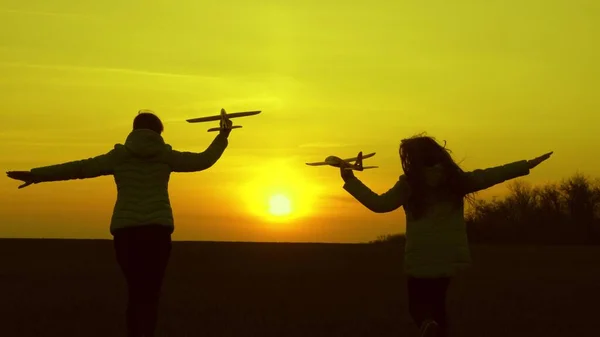 Безкоштовні дівчата грають з іграшковим літаком на заході сонця. Мрії про політ. Здорові діти бігають на сонці з літаком в руці. Щаслива концепція дитинства. Силует дітей, які грають у літаку — стокове фото