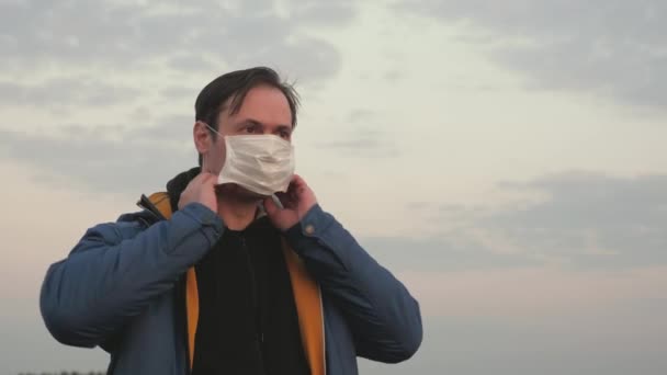 Чоловік одягає медичну маску на вулицю. Захист від вірусів та бактерій. вільний чоловік у захисній медичній масці під час заходу сонця. концепція безпеки та здоров'я, коронавірус N1H1, захист . — стокове відео