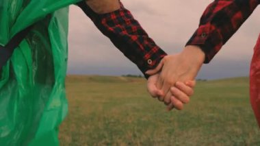 Özgür kadın gezginler vadiden dağlara el ele yürür. Yakın plan. Ağır çekim. Turist kızlar sırt çantalarıyla çok renkli yağmurluklarla seyahat ederler. Takım çalışması gezginleri. macera konsepti.