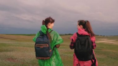 Özgür kızlar tepenin kenarına gider sevinçle ellerini çırp ve mutlulukla zıpla. Sağlıklı kadın turistler sırt çantalarıyla çok renkli yağmurluklarla seyahat ederler. Takım çalışması gezginleri. seyahat kavramı.