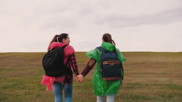 Vrije vrouwen reizigers gaan boven op de berg hand in hand. Langzame beweging. gezonde meisjes toeristen reizen met rugzakken in veelkleurige regenjassen een heuvel beklimmen. teamwerk reizigers. avontuur concept. — Stockvideo