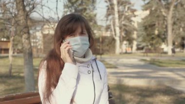 Özgür ve koruyucu maskeli genç bir kadın Avrupa 'da şehir caddesinde akıllı bir telefonla oturuyor. Sokaktaki sağlıklı kız turistler virüslerden korunmak için maske takarlar. konsept sağlık.