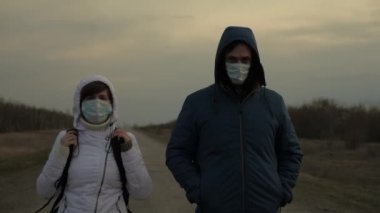 Kadın ve erkek koruyucu maske ve kapüşonlu bir sırt çantasıyla şehirden kaçıyorlar. Şehir dışında yol boyunca yürüyorlar. Virüs ve bakterilere karşı koruma. Güvenlik Konsepti, Coronavirus N1H1