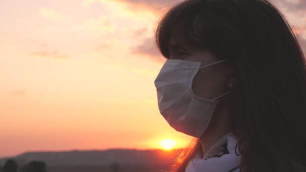 Freie Frau mit einer medizinischen Schutzmaske im Sonnenuntergang. Nahaufnahme. Schutz vor Viren und Bakterien. Gesundheits- und Sicherheitskonzept, Coronavirus N1H1, Virenschutz. Coronavirus-Pandemie. — Stockvideo