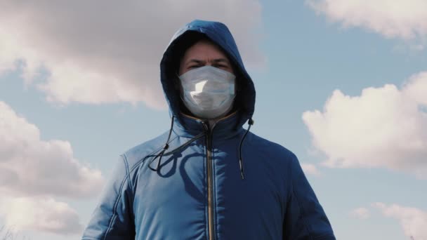 Ένας άντρας με κουκούλα φοράει μια ιατρική προστατευτική μάσκα στο δρόμο σε μια πόλη. Κοντινό πλάνο. έννοια της υγείας και της ασφάλειας, coronavirus N1H1, προστασία από ιούς. έννοια της υγείας και της ασφάλειας. Πανδημία γρίπης. — Αρχείο Βίντεο