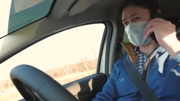 携帯電話を持つ無料の男は車の中でマスクで旅します。ウイルスや細菌から保護します。男の子はアンドロイドを運転して話している。健康な若いです男で保護滅菌医療マスクドライブ車. — ストック動画