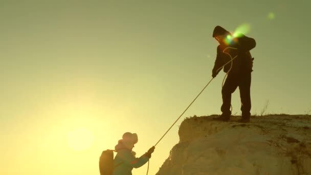 Fri kvinna och man resenär klättrar ett berg. Lagarbete för turister. Klättrare klättrar berg på ett rep. färdas i bergen vid solnedgången. Affärsmän försäkrar varandra. hjälp under svåra omständigheter. — Stockvideo