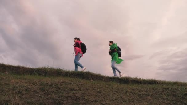 自由女旅行家沿着山顶散步。旅行者的团队合作。探险和旅行的概念。健康的女性游客背着五颜六色的雨衣旅行，暴风雨要来了 — 图库视频影像