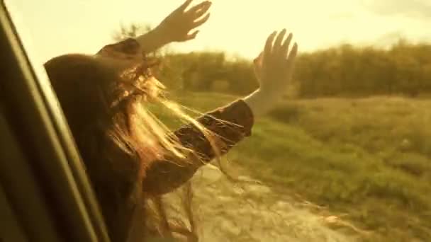 Mujer libre viaja en coche coge el viento con la mano desde la ventana del coche. Chica con el pelo largo está sentado en el asiento delantero del coche, estirando su brazo por la ventana y la captura de resplandor de puesta de sol — Vídeos de Stock