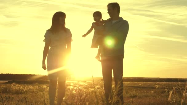 Feliz niño juega con el padre y la madre en el campo. El concepto de familia e hijos. Papá y madre con su amada hija en sus brazos están caminando en el parque al atardecer . — Vídeo de stock