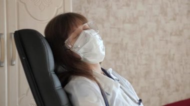 Kadın doktor yorgun, koruyucu tıbbi maske takıyor ve klinikteki gözlükler dinleniyor. Kadın doktor hastanede bir sandalyede uyuyakalmış. Sıhhiyeci gözlerini yorgunluktan ve fazla çalışmaktan kapattı.