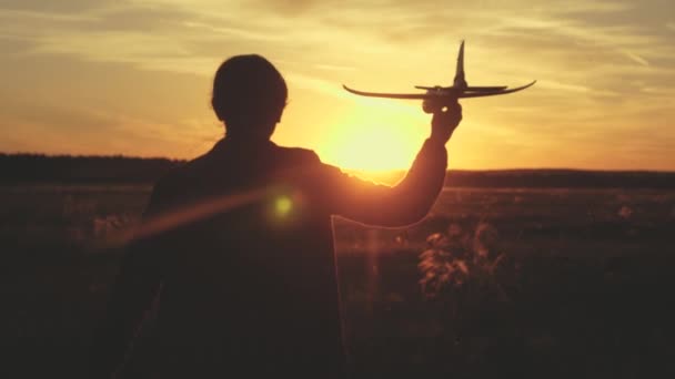 A rapariga quer ser piloto e astronauta. Movimento lento. Menina feliz corre com um avião de brinquedo em um campo sob a luz do pôr do sol. As crianças brincam de avião de brinquedo. sonhos adolescentes de voar e se tornar piloto. — Vídeo de Stock