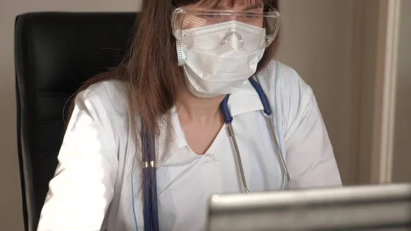 医師は仮想チャットを使用してクライアントと通信します。遠隔医療の概念だ。ノートパソコンで働く白いコートと安全眼鏡の女性医師,オンライン相談と会議. — ストック写真