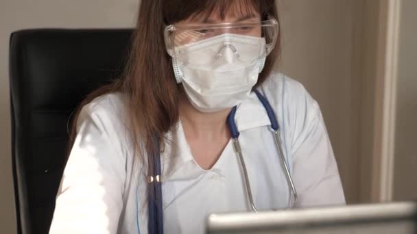 El médico se comunica con un cliente mediante chat virtual. Telemedicina, concepto de atención médica remota. Doctora en bata blanca y gafas de seguridad trabajando en laptop, consulta online y conferencia . — Vídeo de stock