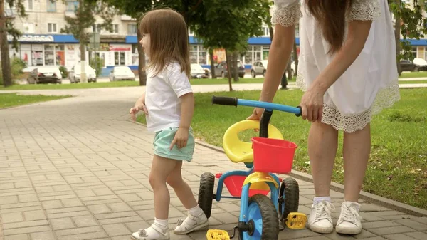 Sağlıklı çocuk bisiklet sürmeyi öğrenir. Ebeveynler ve küçük kızları parkta yürürler. Mutlu anne küçük kızına bisiklet sürmeyi öğretiyor. Anne bebeğiyle dışarıda oynuyor. Mutlu aile ve çocukluk kavramı — Stok fotoğraf