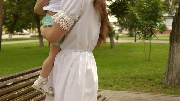 Kleine dochter trekt haar handen naar haar moeder in het park op een bankje. Mama knuffelt gelukkige gezonde baby. Mooie moeder en haar baby spelen in het park. Gelukkige Moederdag Vreugde. concept kindertijd. — Stockfoto