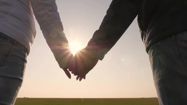 日没時に手をつなぐカップルを愛して。手を友人に伸ばせ。太陽光線が指を通して輝きます。愛、幸福と友情。日没時に男と女の手。ヤシの木を通して. — ストック写真