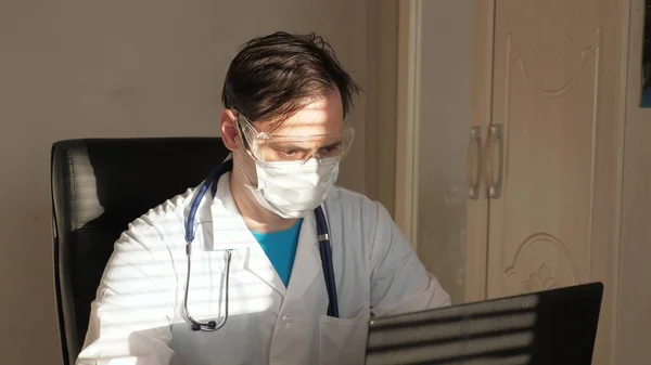 Läkare på kontoret i vit rock och skyddsglasögon arbetar på bärbar dator, online konsultation och konferens. Doktorn kommunicerar med en klient via virtuell chatt. Telemedicin, vård på distans — Stockfoto