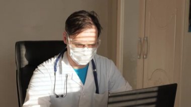 Beyaz önlüklü ve güvenlik gözlüklü bir doktor dizüstü bilgisayar, online danışma ve konferans üzerinde çalışıyor. Doktor sanal sohbet kullanarak bir müşteriyle iletişim kuruyor. Teletıp, uzaktan tıbbi bakım