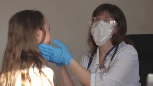 En läkare i medicinsk mask med skyddsglasögon och medicinska handskar undersöker halsen och ögonen på barn. kvinna i vit rock och stetoskop kontrollerar hälsan hos liten flicka. barn på sjukhus avdelning med läkare. — Stockvideo