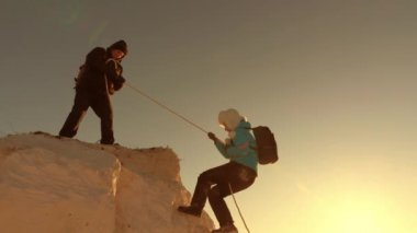 Dağcılar halatla dağa tırmanırlar. Turistlerin ortak çalışması. Neşeli turistler atlayıp ellerini sallıyorlar. Gün batımında dağlara yolculuk. İş adamları birbirlerini sigortalarlar. Zor durumlarda yardım.