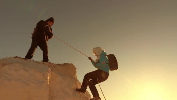 Climbers climb a mountain on rope. joint work of tourists. joyful tourists jump and wave their hands. trip to mountains at sunset. businessmen insure each other. help in difficult circumstances. — Stock Video